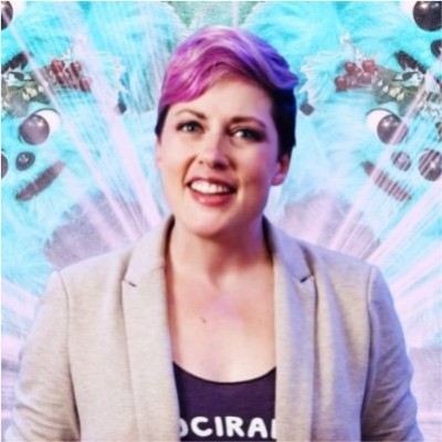 Beth Elderkin, content marketing manager for Informa Connect, smiles in a neutral blazer and black top in front of a purple and blue background. 