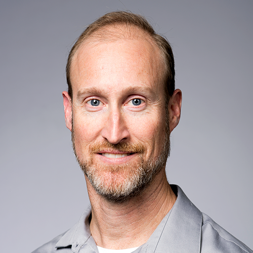 Brian Piper, director of content strategy and assessment at University of Rochester, smiles in a grey shirt in front of a grey background. 