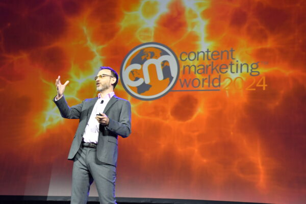 Seth Stephens-Davidowitz is standing on stage wearing a grey suit and pink button down suit. The back is the Content Marketing World 2024 logo.