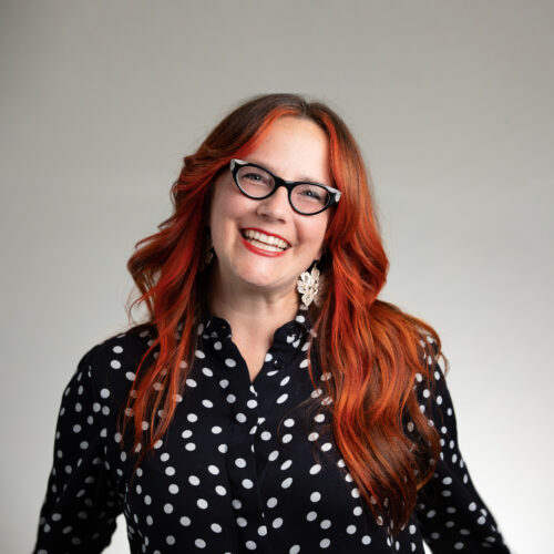 Amy Higgins is wearing black glasses and a black and white polka dot blouse.