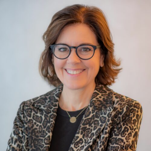 Ann Handley is wearing glasses, a gold necklace, black shirt, and a cheetah blazer.